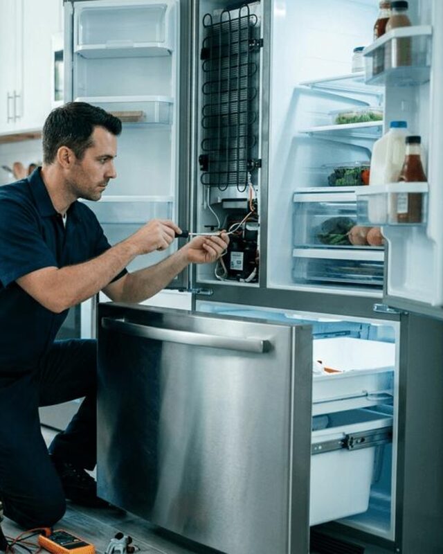 Técnico reparando un nevecón de acero inoxidable en una cocina moderna
